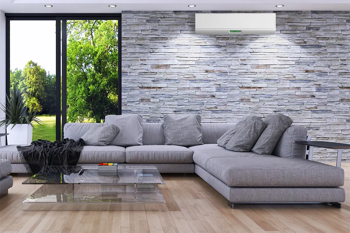 Modernes Wohnzimmer mit grauem Sofa, Steinwand und Klimaanlage über dem Sofa neben großen Fenstern.