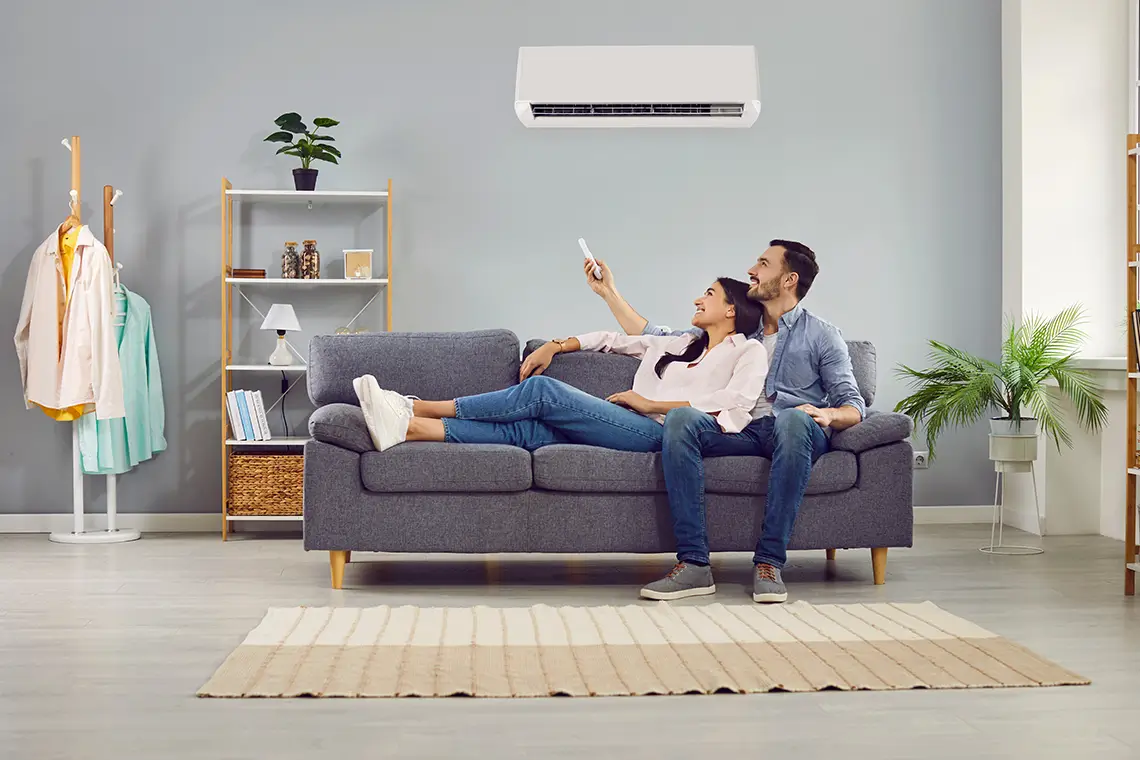 Paar sitzt entspannt zuhause auf dem Sofa und steuert die Klimaanlage per Fernbedienung im Wohnzimmer