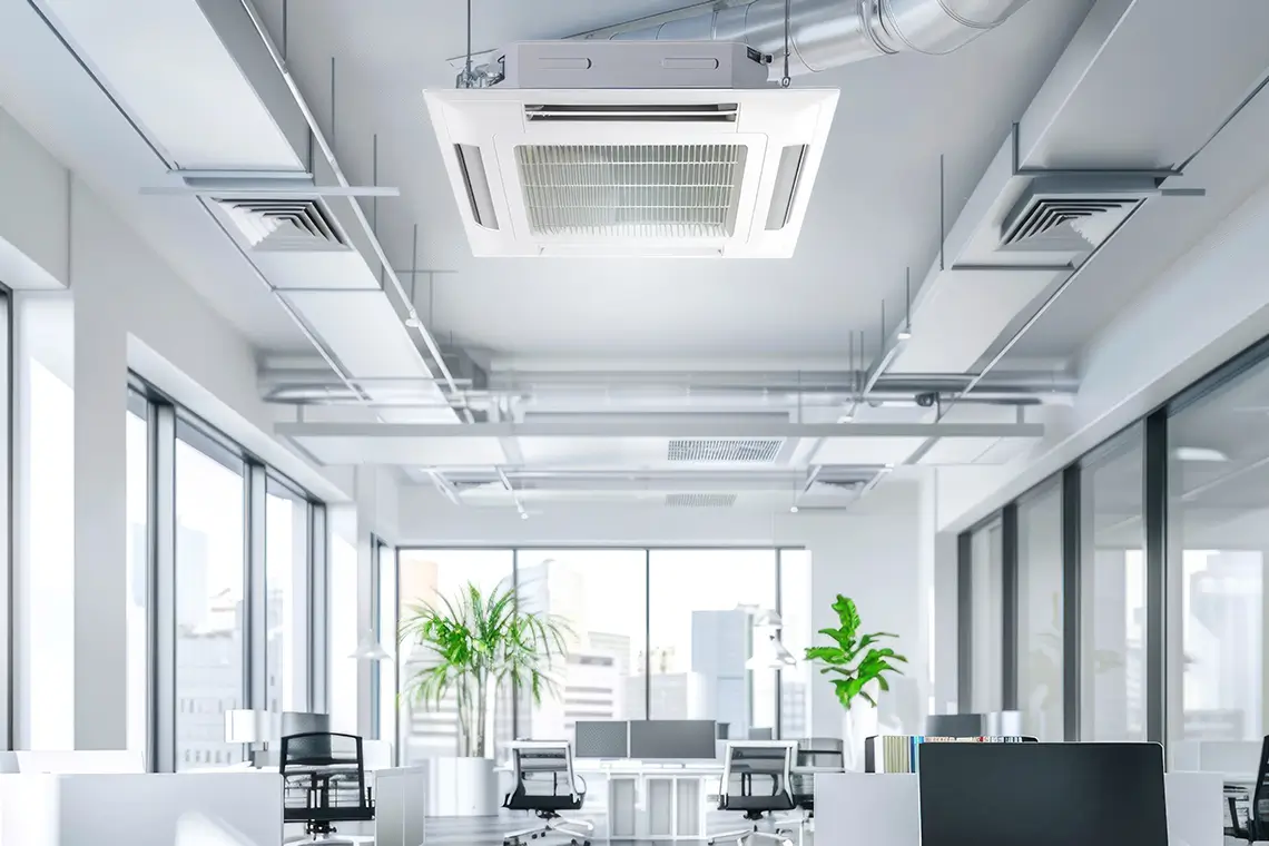 Modernes Großraumbüro mit Deckenklimaanlage, hellen Fenstern, Schreibtischen und grünen Pflanzen.