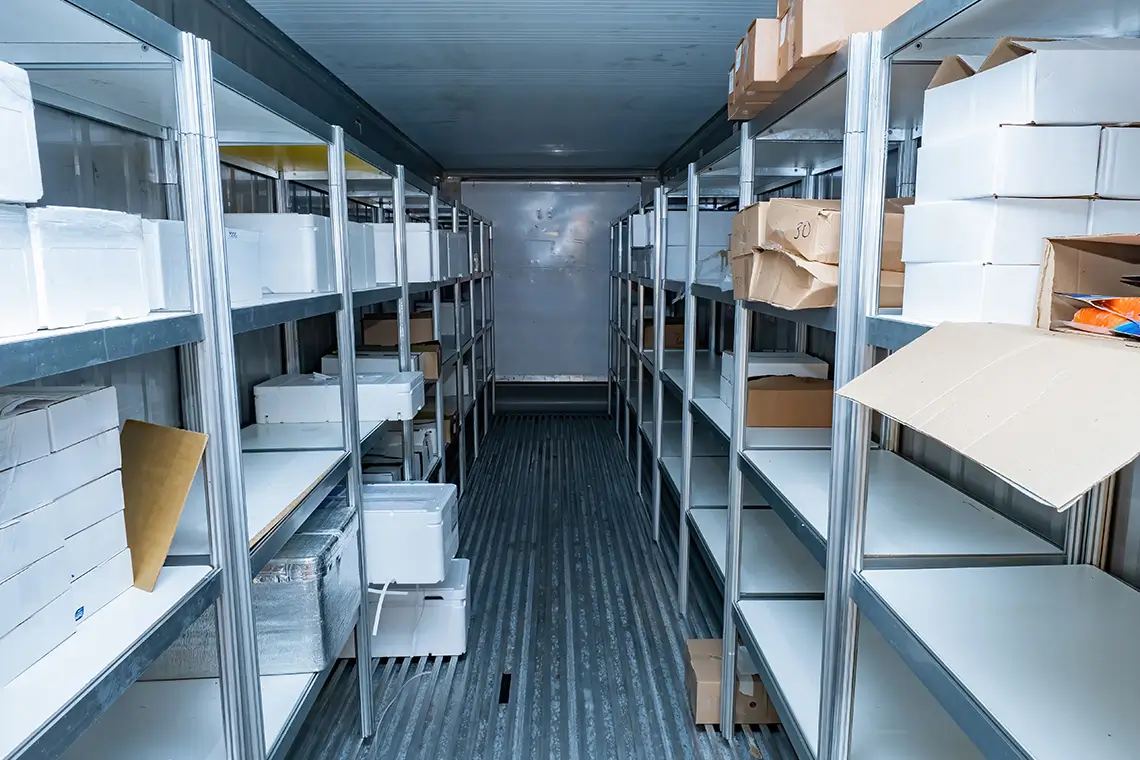 Lagerraum mit Regalen und Kartons in Großküche, genutzt als Tiefkühlanlage für Lebensmittel.