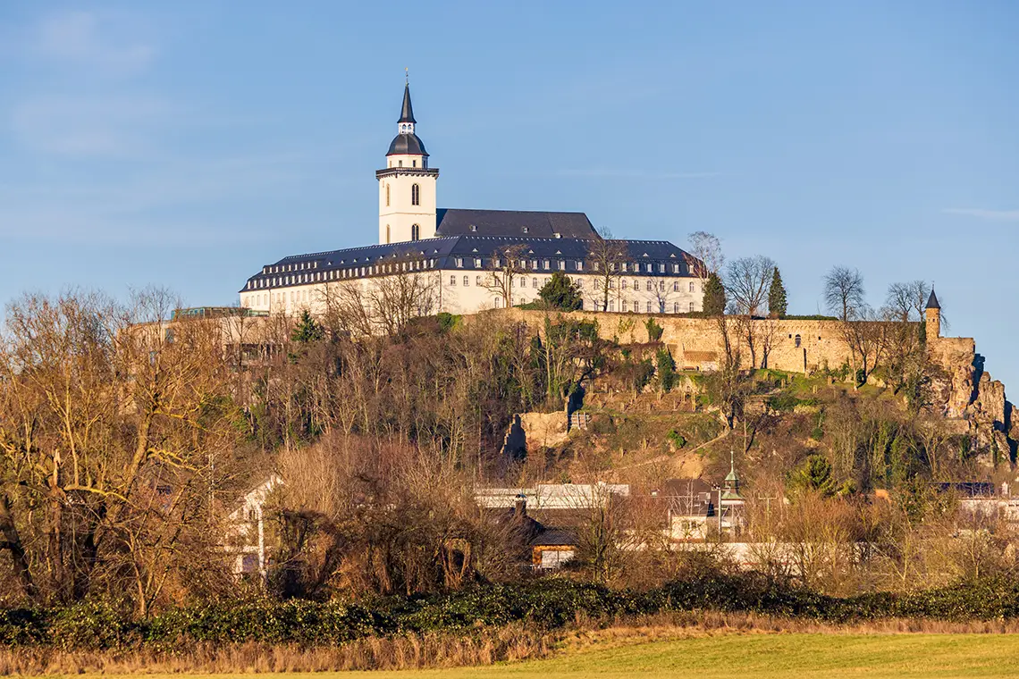 Die Abtei Michaelsberg auf einem Hügel über Siegburg, umgeben von Bäumen und Stadtlandschaft Die Abtei Michaelsberg auf einem Hügel über Siegburg, umgeben von Bäumen und Stadtlandschaft