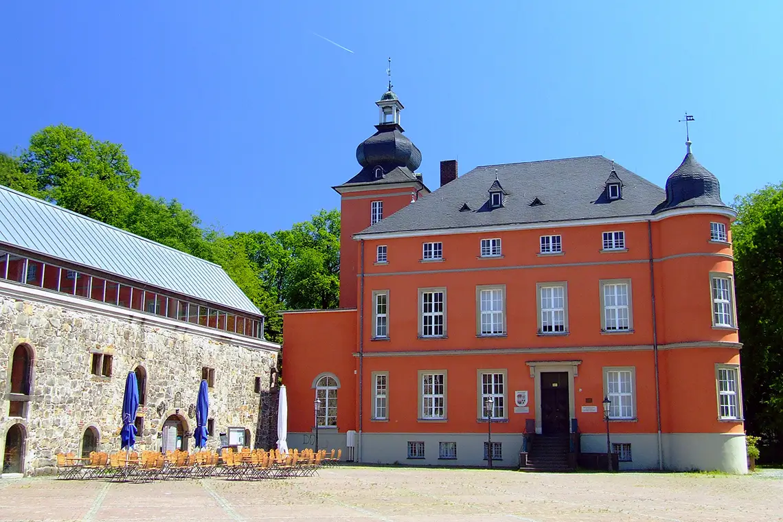 Historisches Schloss Burg Wissem in Troisdorf mit Innenhof, Sitzgelegenheiten und umgebenden Bäumen an einem sonnigen Tag Historisches Schloss Burg Wissem in Troisdorf mit Innenhof, Sitzgelegenheiten und umgebenden Bäumen an einem sonnigen Tag