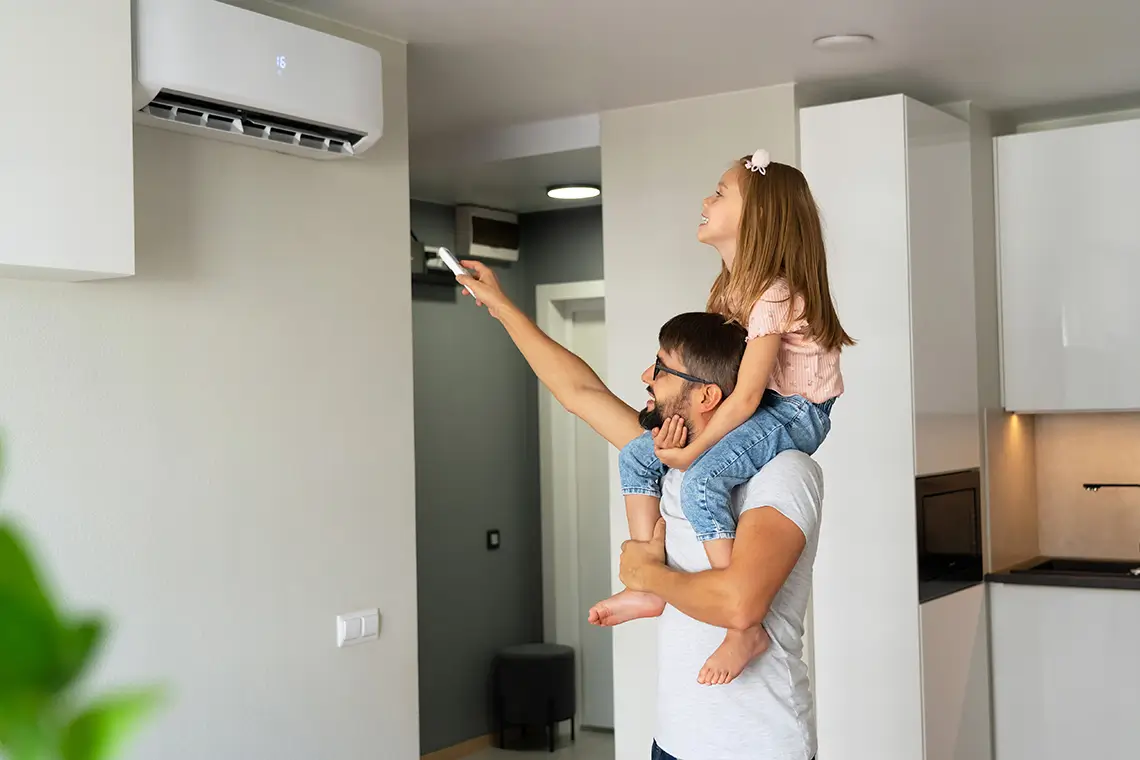Vater mit Tochter auf den Schultern stellt per Fernbedienung eine Klimaanlage in der Wohnung ein Vater mit Tochter auf den Schultern stellt per Fernbedienung eine Klimaanlage in der Wohnung ein