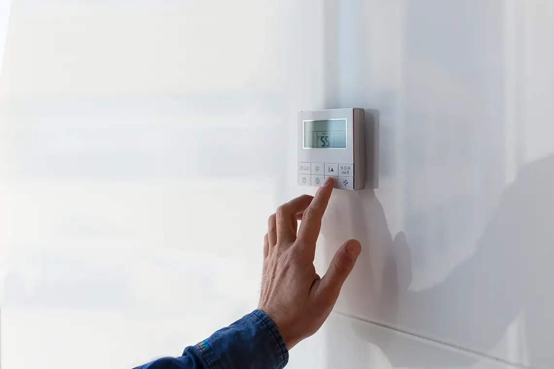 Hand stellt Temperatur an digitalem Klimaanlagen-Thermostat mit Smart Home an der Wand ein Hand stellt Temperatur an digitalem Klimaanlagen-Thermostat mit Smart Home an der Wand ein