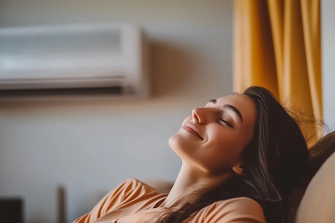 Junge Frau entspannt auf dem Sofa unter einer eingeschalteten Klimaanlage Junge Frau entspannt auf dem Sofa unter einer eingeschalteten Klimaanlage