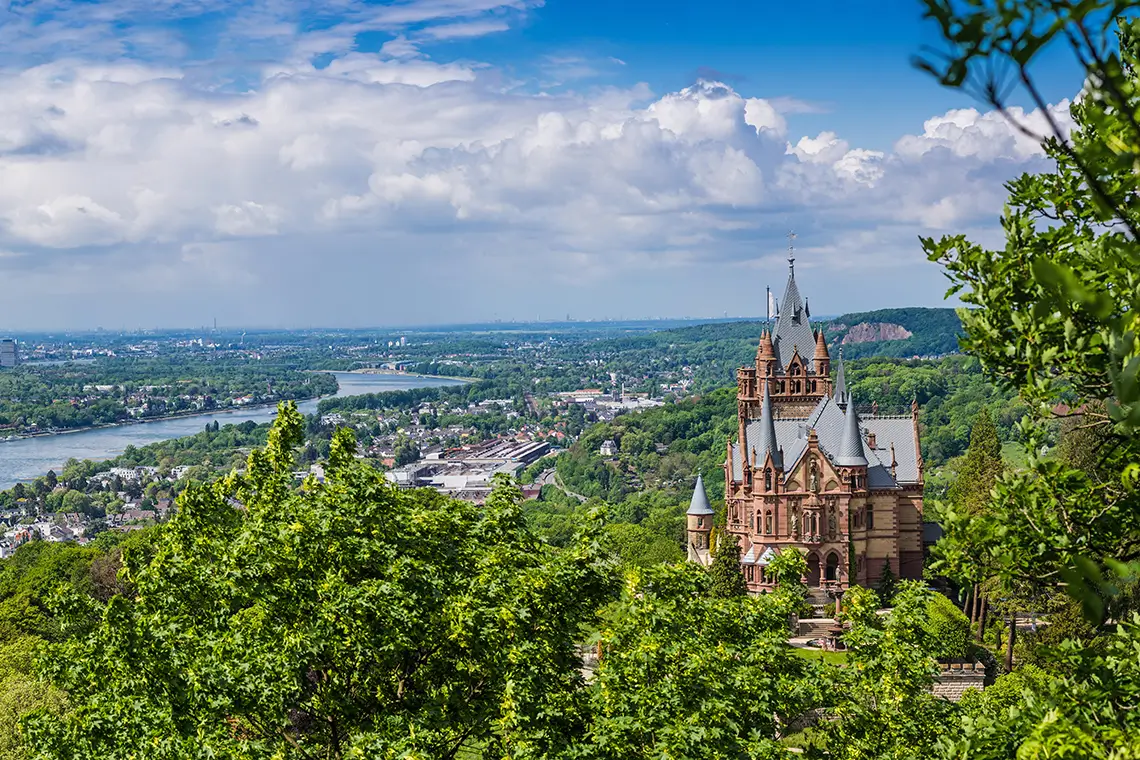 Blick auf Schloss Drachenburg über dem Rhein mit weitem Panorama auf Königswinter und bewaldete Hänge Blick auf Schloss Drachenburg über dem Rhein mit weitem Panorama auf Königswinter und bewaldete Hänge