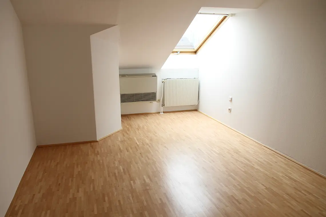 Dachgeschossraum mit Schrägdach, Parkettboden und fest eingebautem Klimagerät an der Wand Dachgeschossraum mit Schrägdach, Parkettboden und fest eingebautem Klimagerät an der Wand